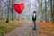 A young man stands in the middle of an autumn landscape and stares at a inflatable helium balloon heart