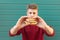 Young man stands on a turquoise background and holds an appetizing burger in his hands