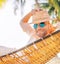 Young man in straw hat and blue sunglasses  lying swinging in cozy hammock sincerely smiling meeting morning sunrise sunlight on