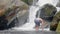 Young man in streaming water from tropical waterfall in wild jungle. Traveling man standing on rocks in flowing river