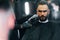 Young man with stylish hairstyle sitting and getting his beard shaved in barber shop