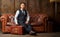 A young man in a suit sits on a leather brown sofa