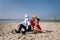 Young man in suit sits with trendy woman on the beach