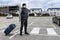 Young man with a suitcase stands on the road in front of the airport building: