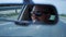 Young man in sunglasses is driving a car. Reflection face in rearview mirror of vehicle.