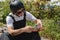 A young man in sunglasses and overalls with a helmet on his head changes his wheels on his longboard under the open sky