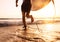 Young man Surfer taking surfboard and running with long surf board to waves on the evening sunset sky background. Active holidays