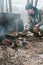 young man survivalist cooks roasts chicken meat food are fried on grill on smoldering coals or ember from a campfire