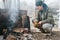 young man survivalist cooks roasts chicken meat food are fried on grill on smoldering coals or ember from a campfire
