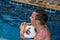 A young man swimming in the pool and holding a ball. Active resting.