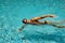 Young man is swimming in a transparent pure water of a pool.