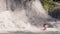 Young man swimming in water from splashing waterfall in tropical jungle. Smiling man bathing in flowing waterfall in