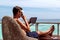 Young man in swimsuit drinking coffee and working on a tablet in a tropical destination