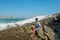 Young man in a T-shirt and blue shorts sitting on a rocky shore. This is a view of man sitting on the rock by the sea