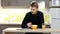 Young man with tablet eating breakfast sitting by table in kitchen at home.