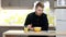 Young man with tablet eating breakfast sitting by table in kitchen at home.