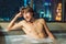 A young man takes a bath against a panoramic window with a view of the night city