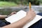 Young man takes notes in a notebook on nature. Man sits by a tree with his back to him, a pencil and a notebook in his hands