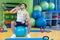 A young man taking a break at the gym sitting on a pilates ball with a bottle of water