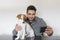 young man taking a picture with his cute small dog. Mobile phone selfie, technology. Pets indoors, white background