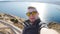 Young man taking travel selfie on trekking excursion day. Against the background of the sea and rocks