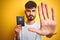 Young man with tattoo wearing Australia Australian passport over isolated yellow background with open hand doing stop sign with