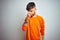 Young man with tattoo wearing orange sweater standing over isolated white background tired rubbing nose and eyes feeling fatigue