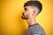 Young man with tattoo wearing striped t-shirt standing over isolated yellow background looking to side, relax profile pose with