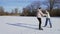 Young man teaches his girlfriend to ride ice skating backwards on frozen lake in forest