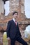 A young man, a teenager, in a classic suit. Pondering is standing in front of the old wall of red brick, putting his hands in his