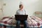 Young man with tin foil hat thinking while using laptop in the bedroom