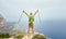 A young man on top of a mountain raised his hands up holding trekking poles