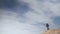 A young man in tourist gear stands on a high sandy slope against the backdrop of a bewitching blue sky, which occupies