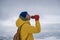 Young man tourist hiker standing on mountain top drinking hot tea from thermos during winter hiking