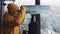 Young man tourist looking through binoculars or telescope on snowy mountains. Travel, nature, hiking conception