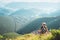 Young man tourist sits on top on hill with beautiful valley pano