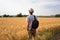 Young man traveler with backpack in hat stands in field at sunset and looks away, concept of freedom of choice, future, concept of