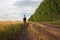 Young man traveler with backpack in hat stands in field at sunset and looks away, concept of freedom of choice, future, concept of