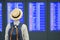 Young man traveler with hat checking flight time, Asian passenger looking to information board in international airport terminal.