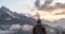 Young man traveler in hood with backpack from behind looking mountain view of the snow capped peaks of Caucasus Mountains in