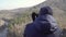 Young man traveler sitting on the rock mountain peak looking with binoculars 4k