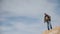 A young man, a traveler, stands on a high slope against the backdrop of a charming sky and uses his cell phone for