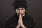 A young man in a turbanl prays with his hands folded in a petition in front of him. Close-up. Black background