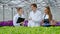 A young man and two women in white coats and black aprons. Three scientists, biologists or agronomists examine and