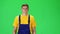 Young man in uniform, yellow t-shirt and blue jumpsuit going and looking forward against green background. Slow motion.