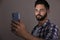 Young man unlocking smartphone with facial scanner on beige background. Biometric verification