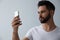 Young man unlocking smartphone with facial scanner on grey background. Biometric verification