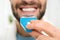 Young man using teeth whitening device on light background