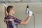 Young man in usual clothing and work gloves fixing drywall suspended ceiling to metal frame using electrical screwdriver on