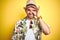 Young man on vacation wearing hawaiian flowers shirt and summer hat over yellow background doing ok gesture with hand smiling, eye